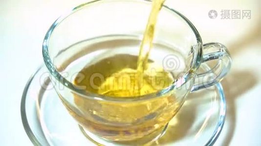 在白色背景特写镜头上，将茶壶中的红茶香气注入一个匹配的透明玻璃茶杯。视频