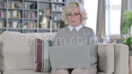 严肃的老妇人坐在沙发上用笔记本电脑视频