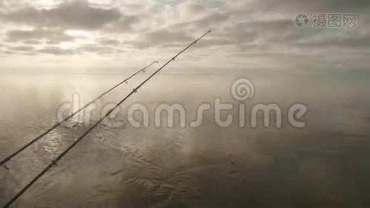 三根鱼竿在水面上的景色，钓船上挂着尖嘴。 多云的天空在背景上。视频