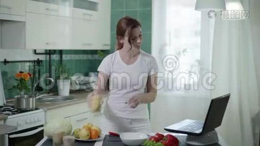 年轻的女人在厨房里做健康的食物，女孩用勺子测量麦粥，看着笔记本电脑的食谱视频