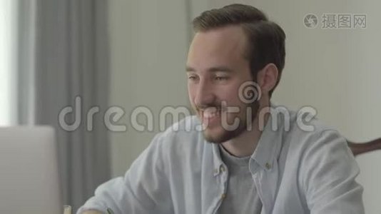 一个年轻英俊的男人坐在办公室的电脑前微笑点头的肖像。 上班族视频