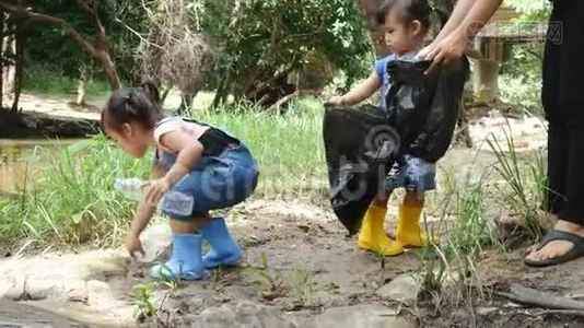 一个亚洲小孩，带着一家人在一条公共河流的边缘用黑色袋子捡起垃圾和塑料瓶。视频