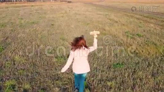 女孩跑过田野，拿着飞机，模拟飞行。 秋天晴朗的一天。 户外娱乐视频