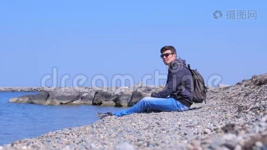 人类旅游旅行者坐在石滩上，把石头扔进水里。视频