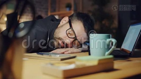 当同事们工作时，精疲力竭的经理晚上睡在办公室的桌子上视频