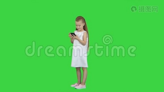 可爱的小女孩微笑，用手机在绿色屏幕，色度键视频