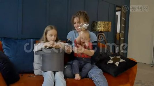 年轻的母亲、女儿和儿子在家里坐在橙色的沙发上庆祝节日或生日视频