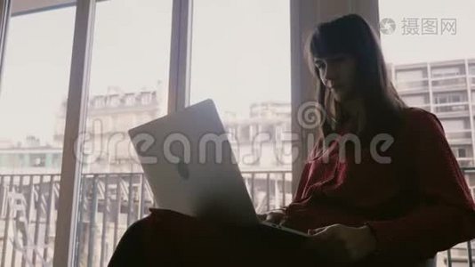 快乐美丽的年轻女商人微笑着使用笔记本电脑在巴黎的公寓窗口，火车经过。视频