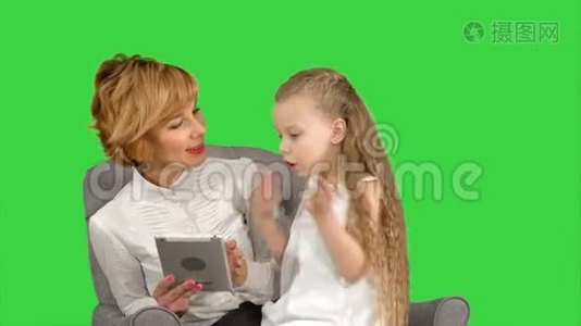 年轻的母亲和女儿坐在一起，看着绿色屏幕上的平板电脑，Chroma键视频