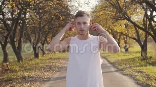 穿着运动服的年轻白种人男孩戴上耳机，开始在秋季公园跳绳锻炼。 田径视频