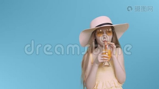年轻的少女戴着黄色眼镜，戴着帽子，在蓝色屏幕上喝鸡尾酒。视频