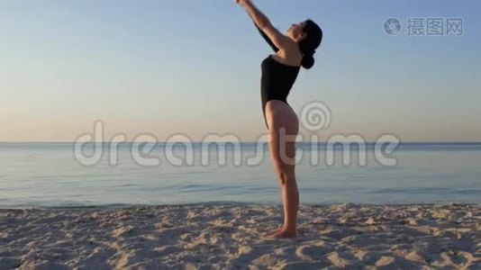 运动的女人穿着黑色紧身衣，在令人惊叹的日出时在海边做瑜伽。 健身、运动、瑜伽和健康生活方式视频