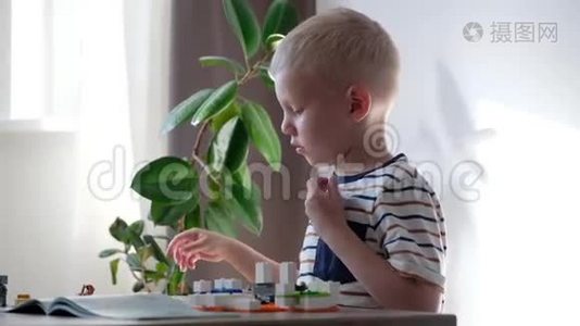 可爱的男孩6岁在家里的桌子上玩五颜六色的塑料玩具砖。视频
