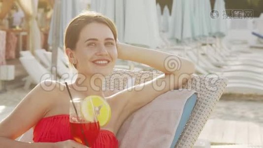 可爱的年轻女子在海滩晒日光浴的时候喝着鸡尾酒视频