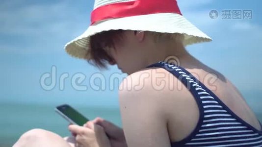 年轻的美女使用智能手机、戴着复古帽子、穿着蓝色和白色泳衣的信使应用程序输入文字视频