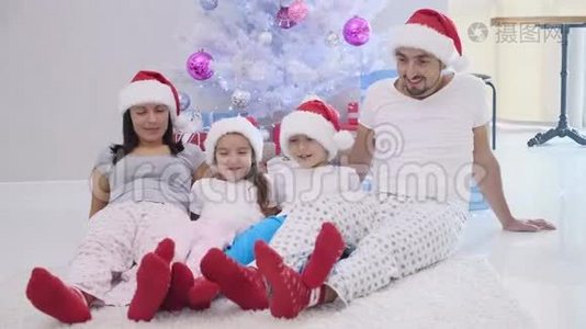 快乐的父亲、母亲、兄弟姐妹准备过圣诞节，坐在杉树附近的地毯上，戴着圣诞帽视频