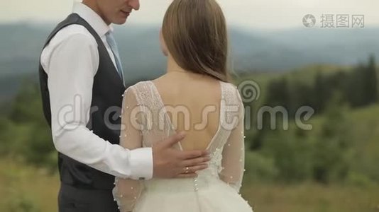 新郎在山丘附近抚摸新娘的背。新婚夫妇视频