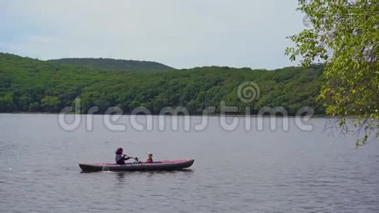 一个年轻人和他的小儿子坐在湖或海湾里的一艘充气大皮艇上视频