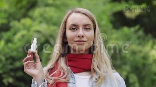 站在城市公园里，戴着红领巾手里拿着过敏性鼻子喷的美丽微笑女子的画像视频