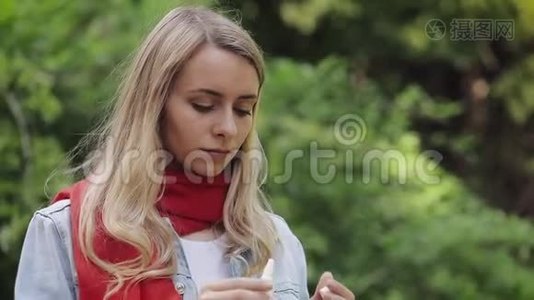 穿着红色围巾喷鼻喷雾的年轻女子站在城市公园。 保健治疗概念概念视频