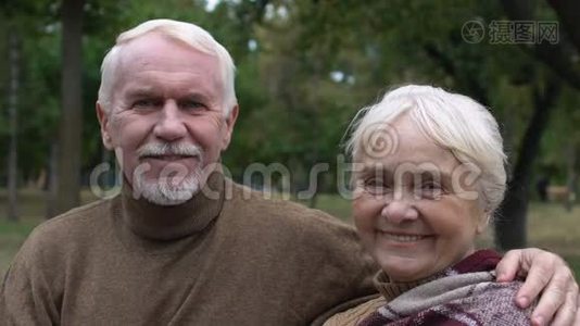 微笑成熟的夫妇坐在公园的长凳上拥抱，社保视频