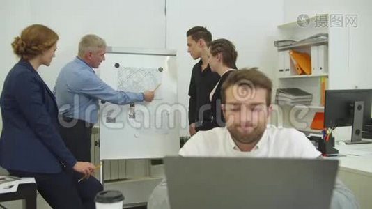 疲倦的人在笔记本电脑上工作，工作的同事看着他在办公桌上的分居计划视频