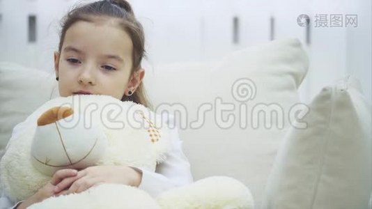 小迷人的女孩心烦意乱。 她坐在沙发上拥抱她的大毛绒朋友。视频