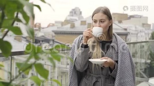 穿着毯子的年轻白人妇女，喝着茶或咖啡。站着喝饮料的女孩看向别处视频