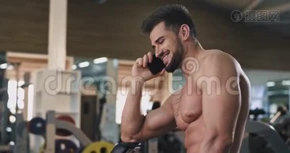 健身运动结束后，一个身材健美的年轻人在一个大型的体育课上打电话视频