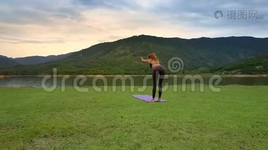 Flycam侧景女孩保持瑜伽姿势在湖边山岸视频