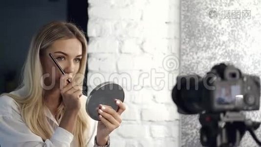 美女vlogger正在用镜子把她的眉毛画在照相机上视频