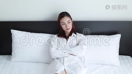 可爱的亚洲女人穿着白色睡衣在床上想着什么。视频
