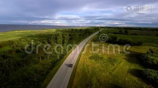 在经过一片绿色森林的大海背景下，一辆孤独的汽车的空中景色视频