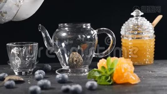 茶叶酿造。 绿色中国茶花玻璃茶点在木制背景。 蓝莓，玻璃罐加蜂蜜。 浇注视频