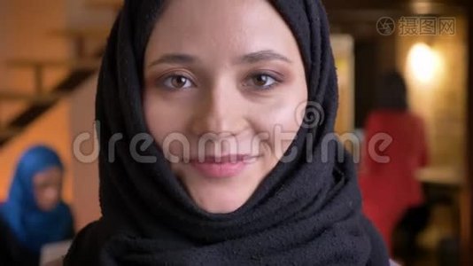 年轻幽默的穆斯林女性办公室工作人员戴着黑色头巾，看着镜头，开心地笑着视频