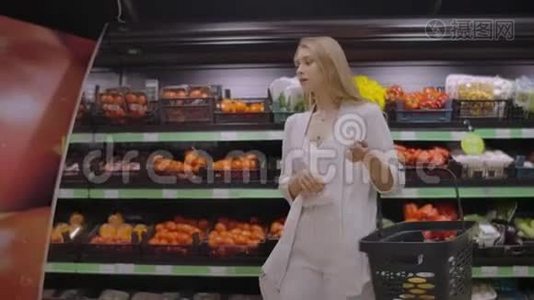 一个漂亮的女人走过超市，手里拿着一个篮子，看着水果的架子。 购买新鲜食品视频