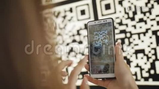 一位使用智能手机的女士在一个现代化公园的凉亭互动墙上扫描大型QR码视频