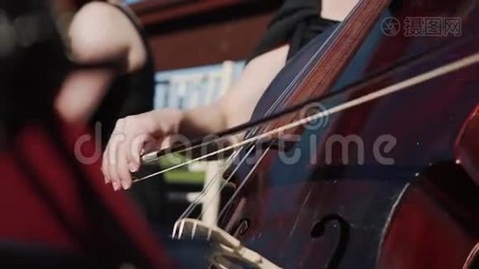 女性手演奏大提琴与弓，户外管弦乐队。视频