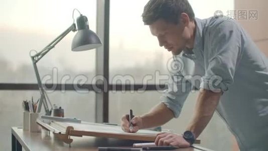 一个人是一个年轻的现代建筑师，坐在桌子旁，画一个建筑的平面图，并制定一个设计，坐在里面视频