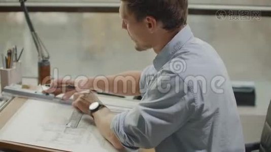 一位男性建筑师坐在一张桌子旁画出一个建筑的平面图，从事设计开发，坐在视频