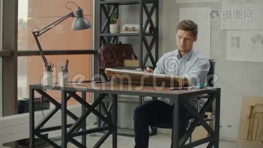 一位男性建筑师坐在一张桌子旁画出一个建筑的平面图，从事设计开发，坐在视频