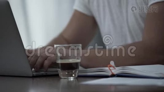 穿着白色t恤、手提电脑和文件在家或办公室喝咖啡的无名男子。 他就是视频