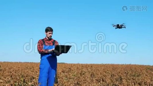 人类使用飞行无人机，同时在一个有庄稼的田野上工作。视频