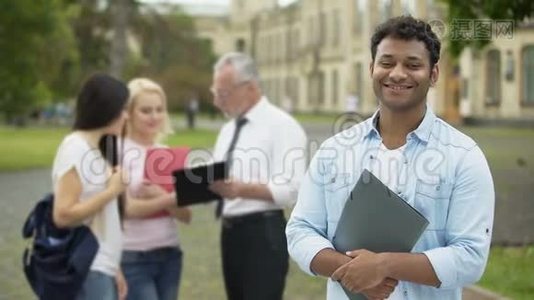 快乐的西班牙裔学生站在大学附近，看着镜头，教育视频