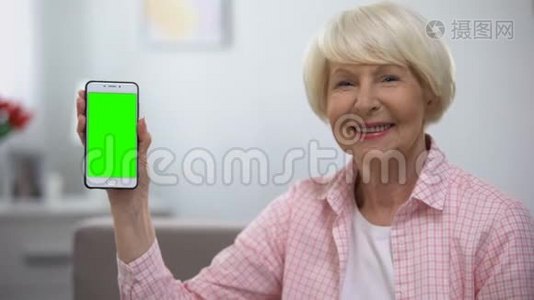 年轻的老妇人在相机上显示带有绿色屏幕的智能手机视频