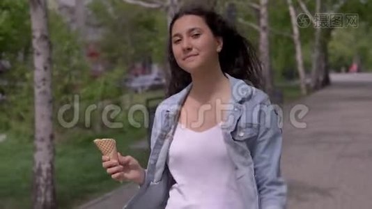 一个漂亮的年轻女孩走在街上，在炎热的夏天吃冰淇淋，同时心情很好。视频