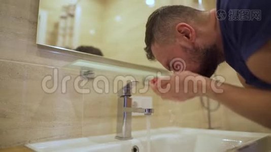 早上的卫生。 男人在浴室里用清水洗脸。 慢动作视频