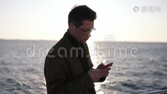一位穿着棕色外套、戴着时髦眼镜、穿着智能手机发短信或在网上冲浪的白种人的肖像。视频