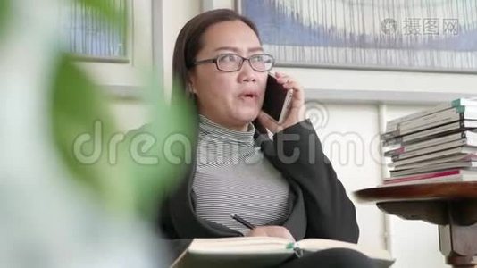 女人在家庭办公室用智能手机写笔记。视频