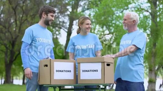 快乐的志愿者奉献高五，捐赠箱在桌上，慈善活动视频